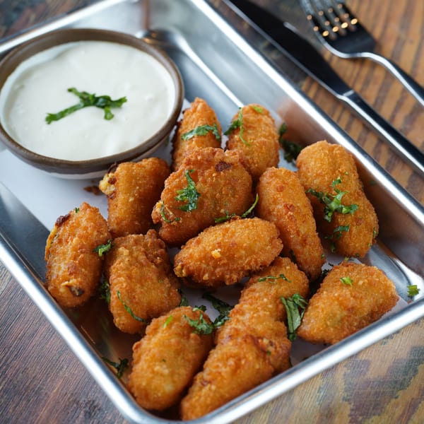 Golden-brown fried appetizers with green garnish and a side of creamy white dipping sauce.