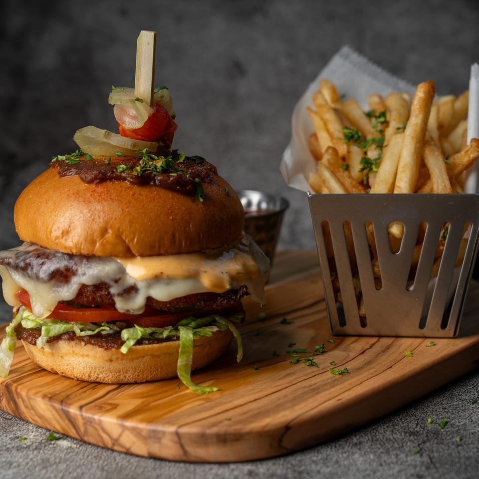 A gourmet burger with melted cheese, lettuce, tomato, and caramelized onions, served with fries.