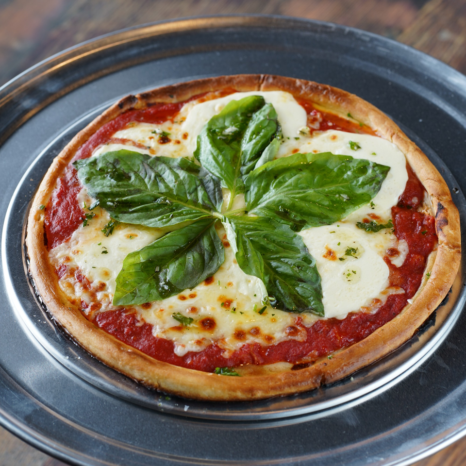 A freshly baked Margherita pizza with melted mozzarella, red sauce, and basil leaves on a metal tray.