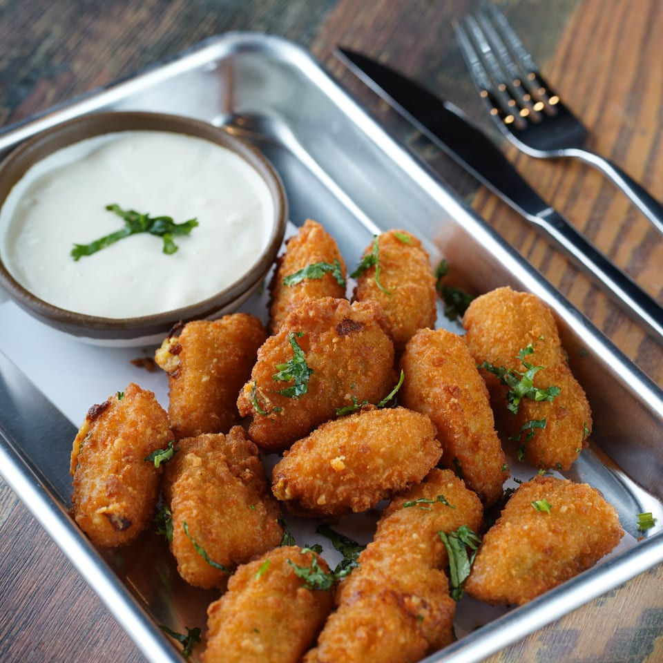 Crispy fried appetizers with green herbs and a side of creamy white dipping sauce on a metal tray.