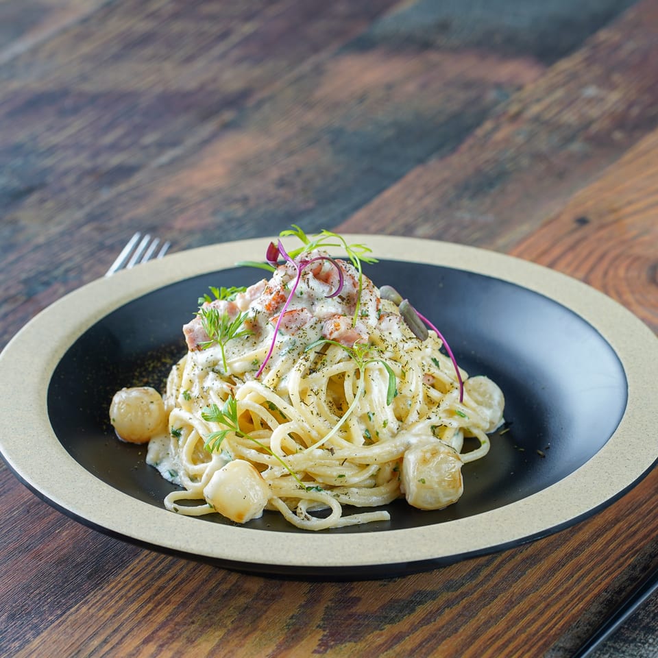 Creamy spaghetti carbonara with bacon, herbs, and pearl onions on a black and beige plate.
