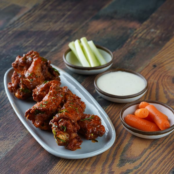 Spicy chicken wings with celery sticks, baby carrots, and ranch dressing on a wooden table.