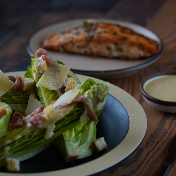 Caesar salad with croutons and parmesan, with a salmon fillet and dressing in the background.