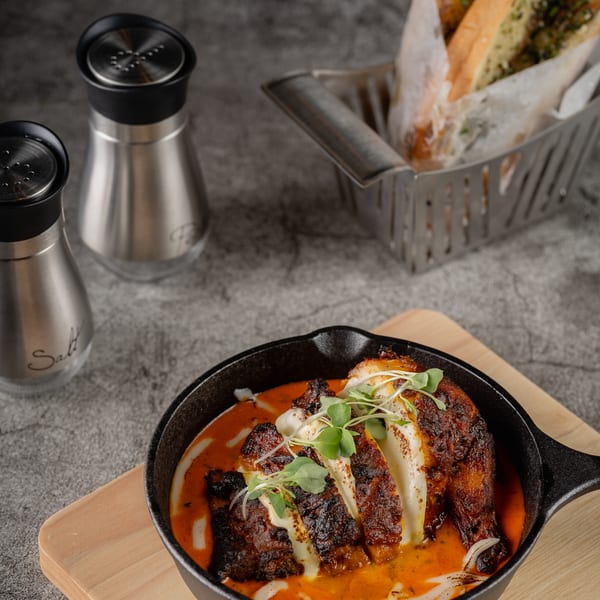 Grilled chicken in a cast iron skillet with red sauce, microgreens, and salt and pepper shakers.