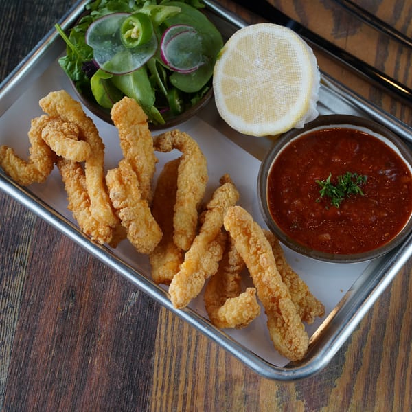 Crispy fried calamari with a side of marinara sauce, lemon, and a small green salad.