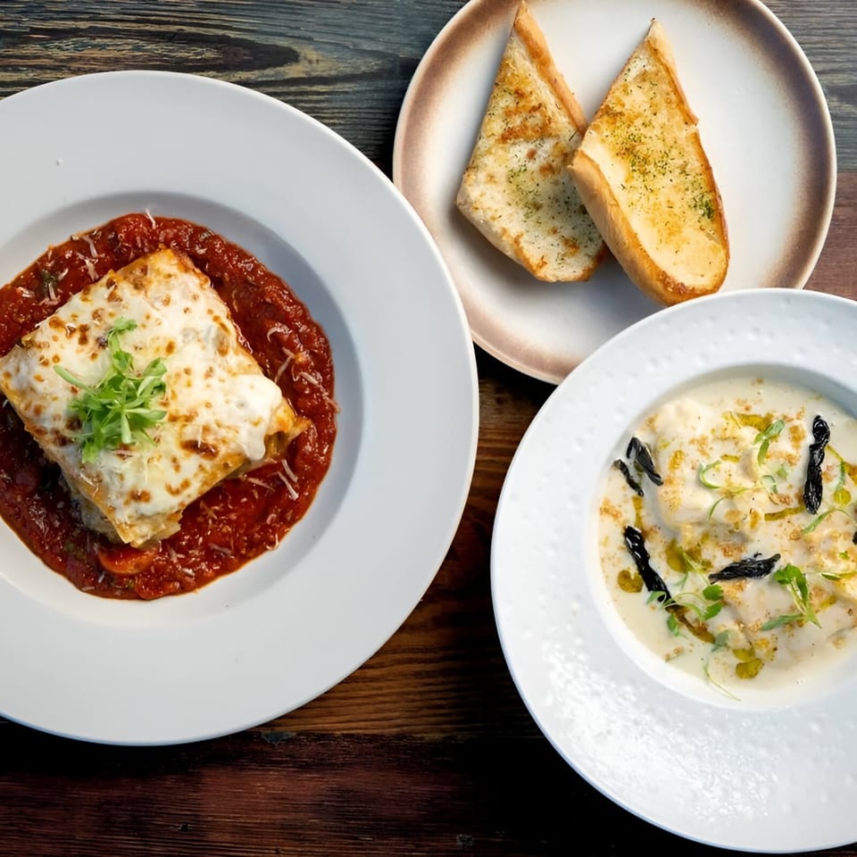 Lasagna, garlic bread, and a creamy pasta dish with mushrooms and herbs on a wooden table.