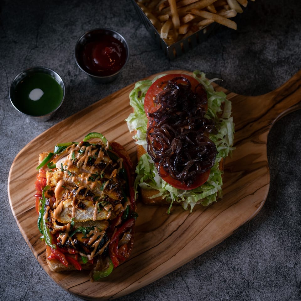 Two open-faced sandwiches, one with chicken and peppers, the other with lettuce, tomato, and onions.