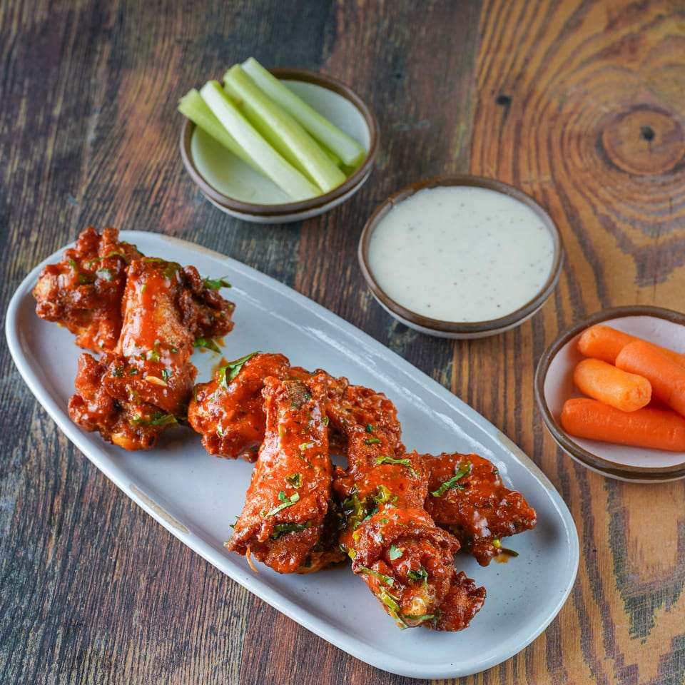 Spicy chicken wings with ranch, celery, and carrots on a wooden table at The Lounge @2nd.