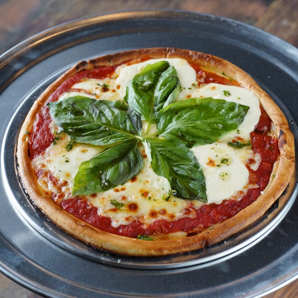 A freshly baked Margherita pizza with melted mozzarella, red sauce, and basil leaves on a metal tray.